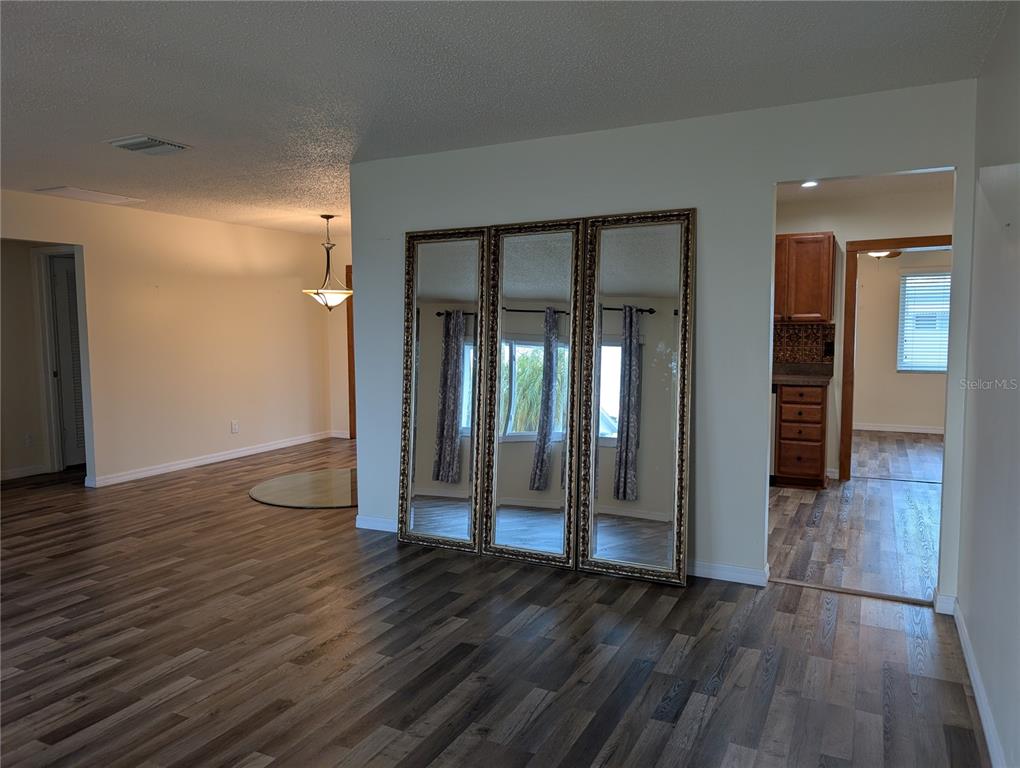 A living area features wood-look flooring, a large three-panel mirror, and an adjacent kitchen doorway — 10188 45TH STREET N UNIT 2, PINELLAS PARK, FL