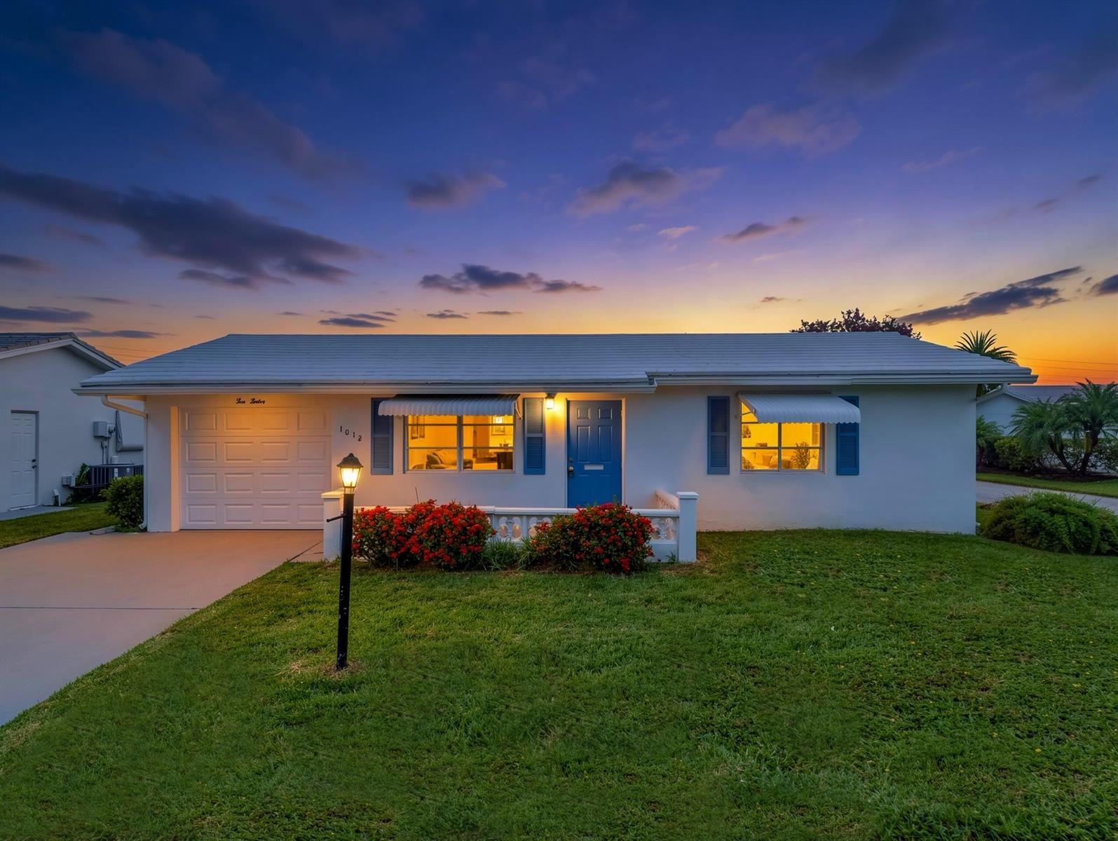 A single-story white house with a blue door, garage, and front lawn at sunset — 1012 SW 17th Street, Boynton Beach FL 33426, BOYNTON BEACH, FL
