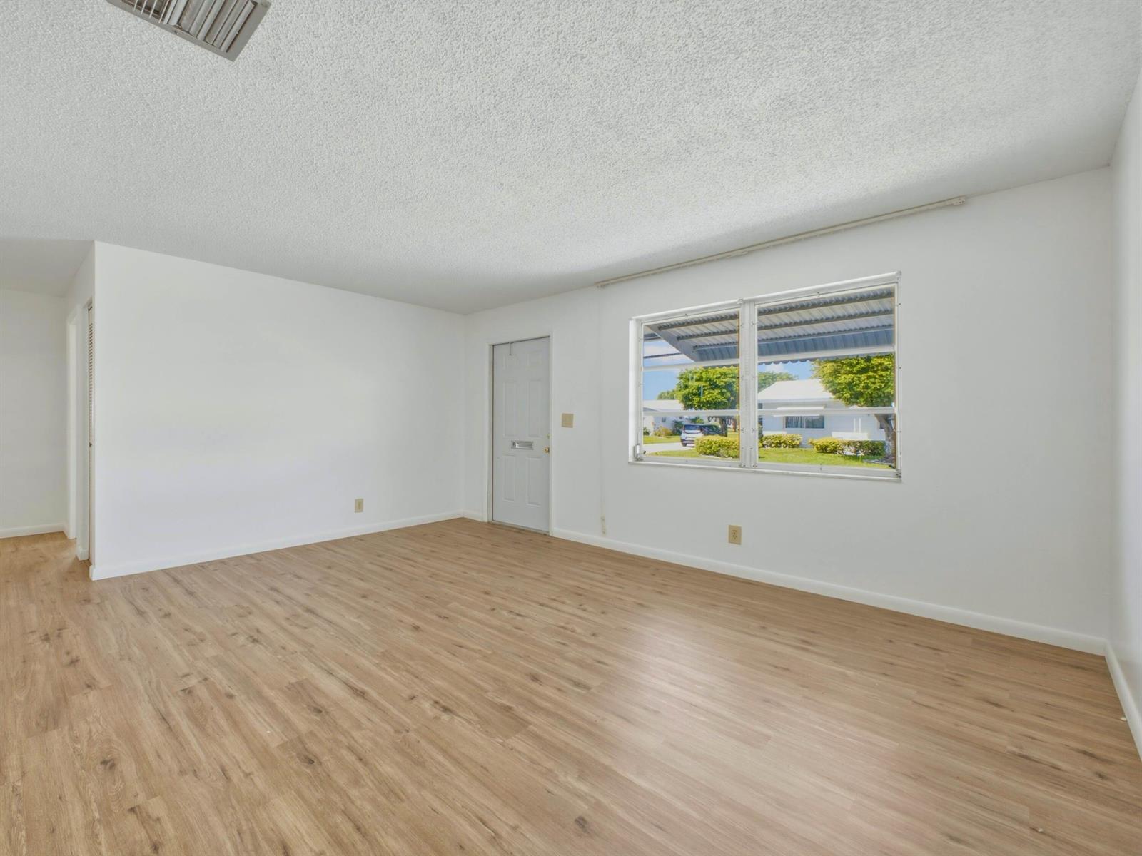 An empty room with white walls, light wood-look flooring, a window, and a door — 1012 SW 17th Street, Boynton Beach FL 33426, BOYNTON BEACH, FL