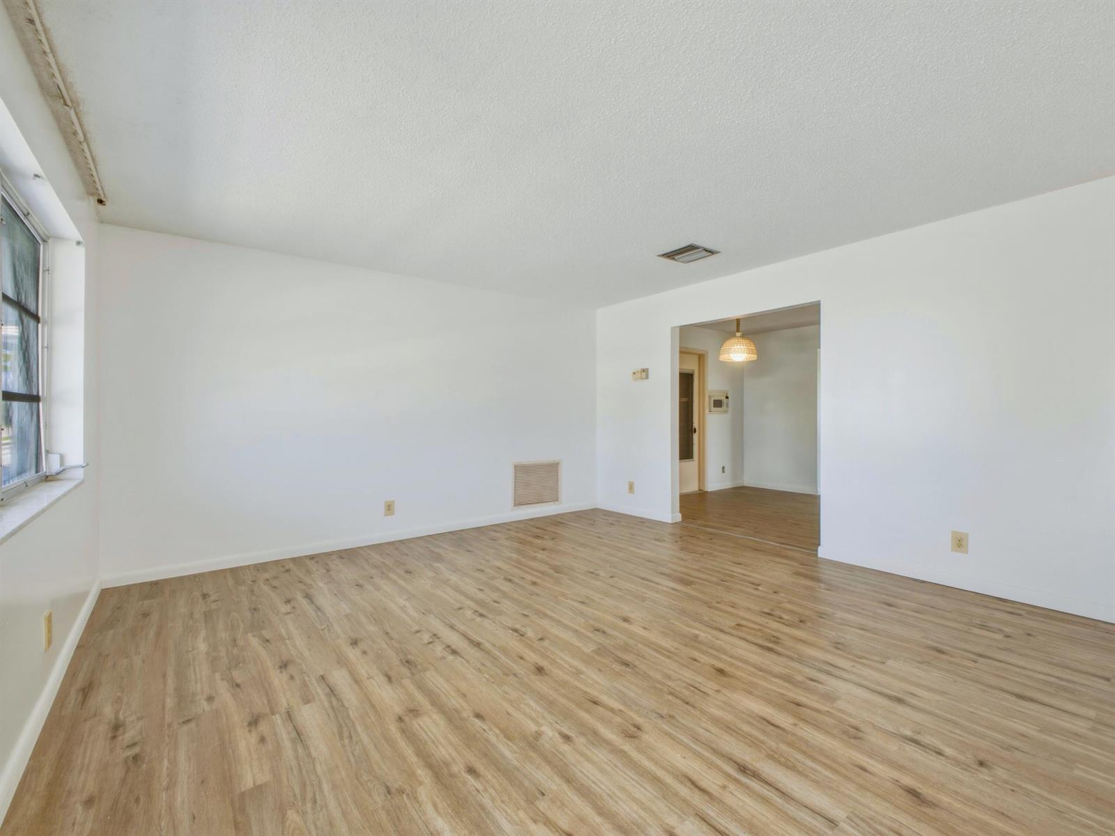An empty living room with white walls, light wood-look flooring, and a doorway to another room — 1012 SW 17th Street, Boynton Beach FL 33426, BOYNTON BEACH, FL