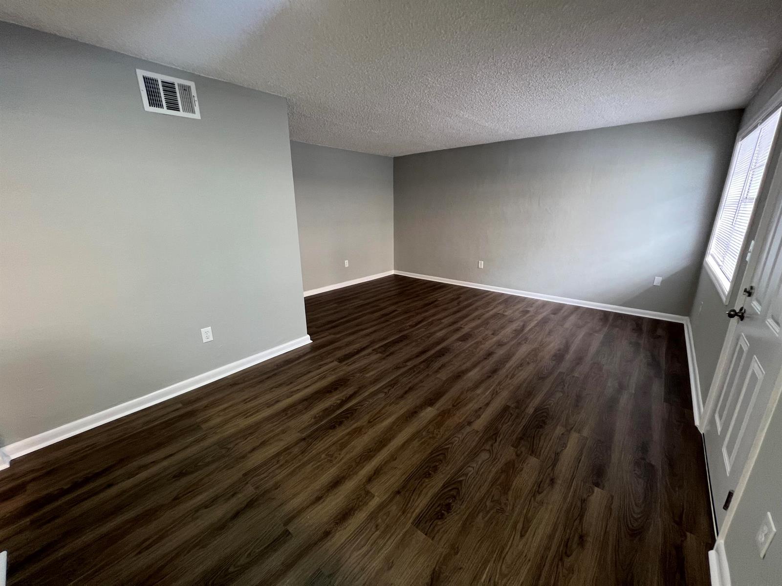 An empty room features gray walls, dark wood-look flooring, and a white door — 2561 NW 135th Street # 3, Opa-Locka FL 33167, OPA-LOCKA, FL