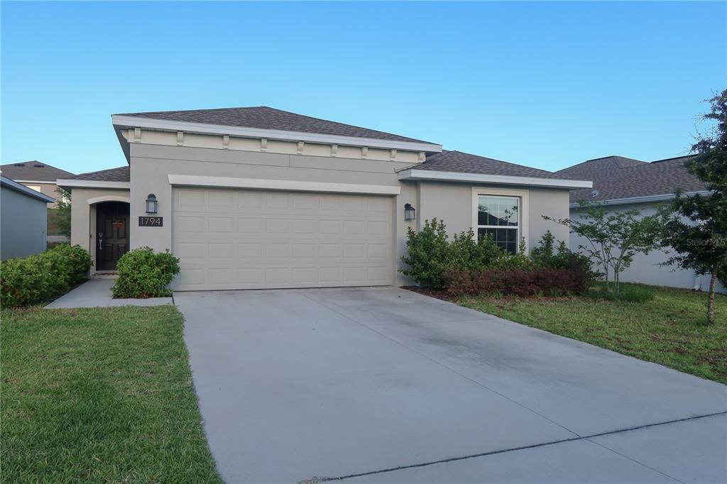 A single-story house with a gray stucco exterior, a two-car garage, and a concrete driveway — 1794 PERCH HAMMOCK LOOP, GROVELAND, FL