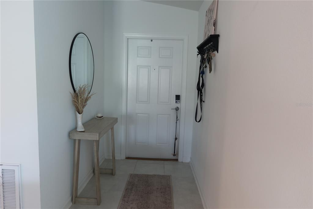 A bright entryway features a white door, a console table, a mirror, and tile flooring — 1794 PERCH HAMMOCK LOOP, GROVELAND, FL