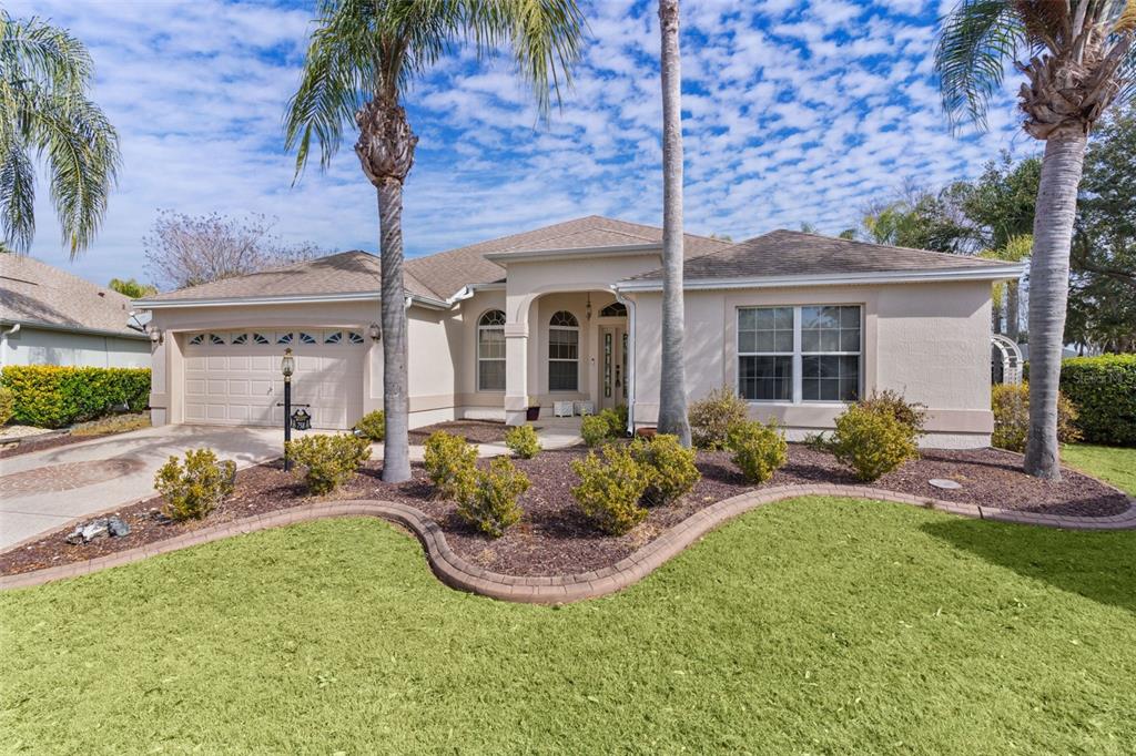A single-story beige house with a two-car garage, palm trees, and a landscaped front yard — 758 MOORE TERRACE, THE VILLAGES, FL