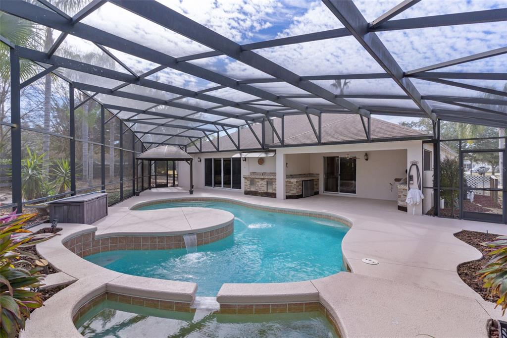 A screened-in pool area features a tiered swimming pool with a waterfall and outdoor kitchen — 758 MOORE TERRACE, THE VILLAGES, FL
