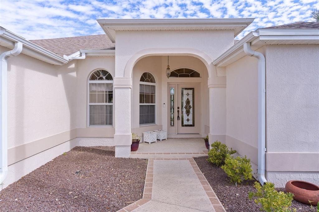 The exterior of a beige stucco house features an arched entryway and a paved walkway — 758 MOORE TERRACE, THE VILLAGES, FL