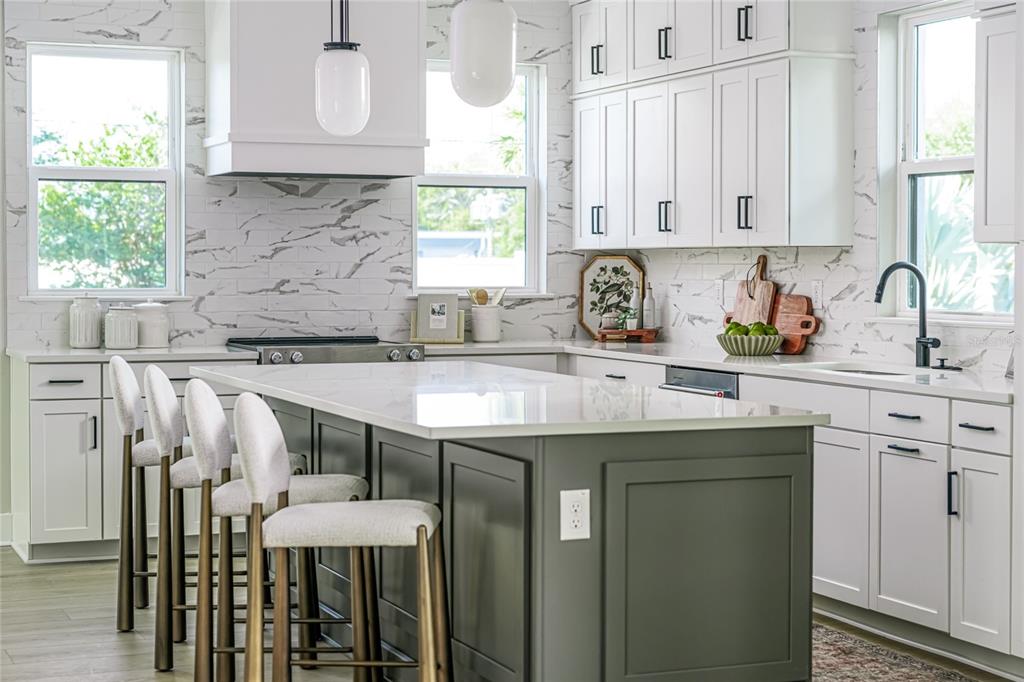 A modern kitchen features a dark gray island, white cabinetry, marble-patterned backsplash, and bar stools — 3009 1ST AVENUE N, ST PETERSBURG, FL
