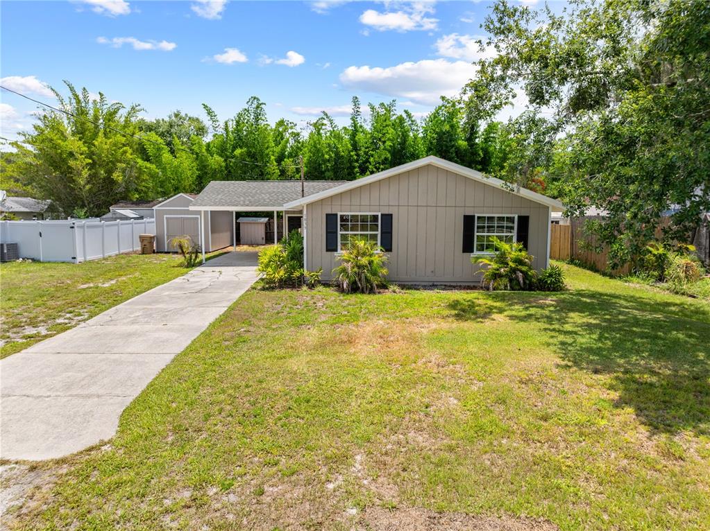 A single-story house with a carport, beige siding, and a front lawn under a sky — 1839 BURTON DRIVE, ST CLOUD, FL