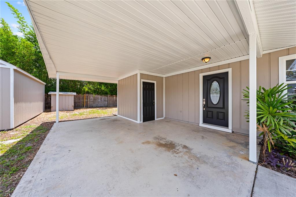 A covered concrete carport features a black front door and a small storage closet — 1839 BURTON DRIVE, ST CLOUD, FL