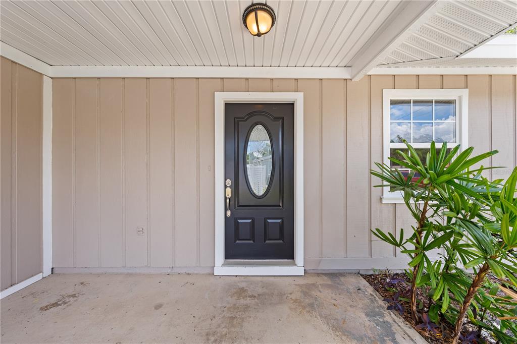 A tan house exterior features a black front door with an oval window and porch — 1839 BURTON DRIVE, ST CLOUD, FL