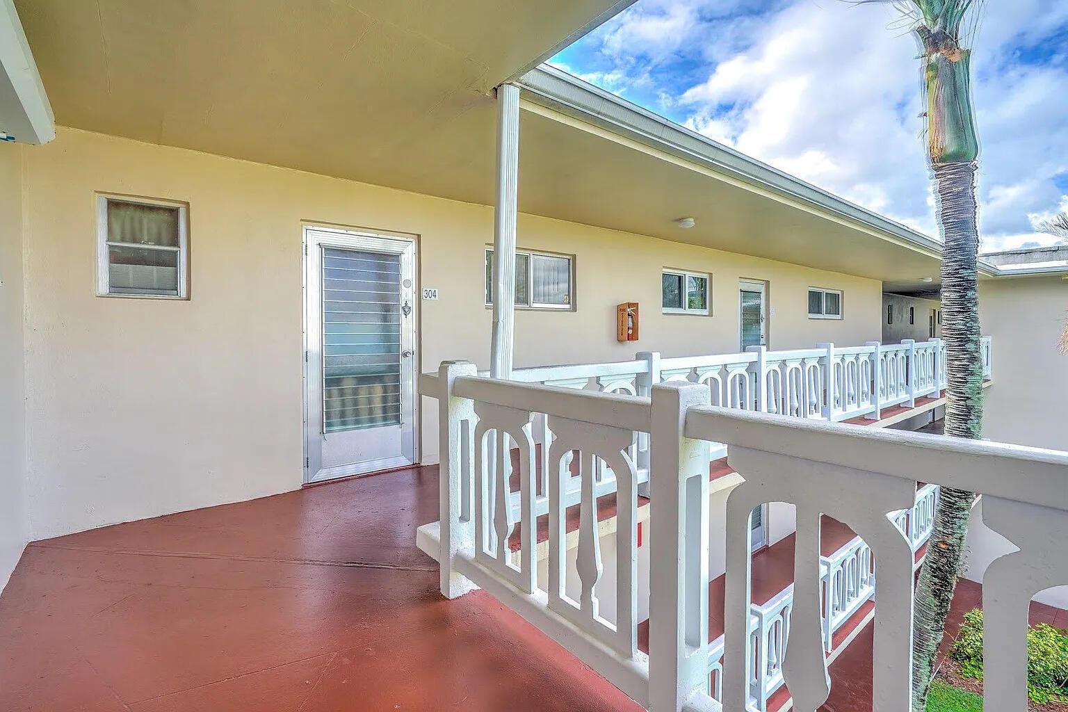 An outdoor walkway with a white railing leads to the entrance of unit 304 — 2606 Garden Drive S # 304, FL 33461, FL