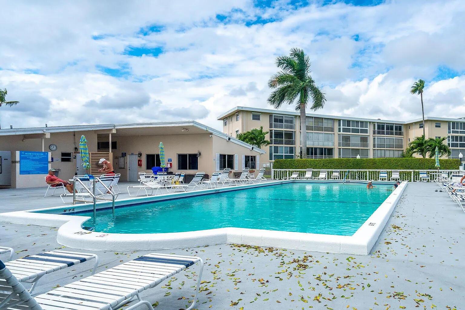 A rectangular swimming pool sits on a concrete deck surrounded by lounge chairs and buildings — 2606 Garden Drive S # 304, FL 33461, FL