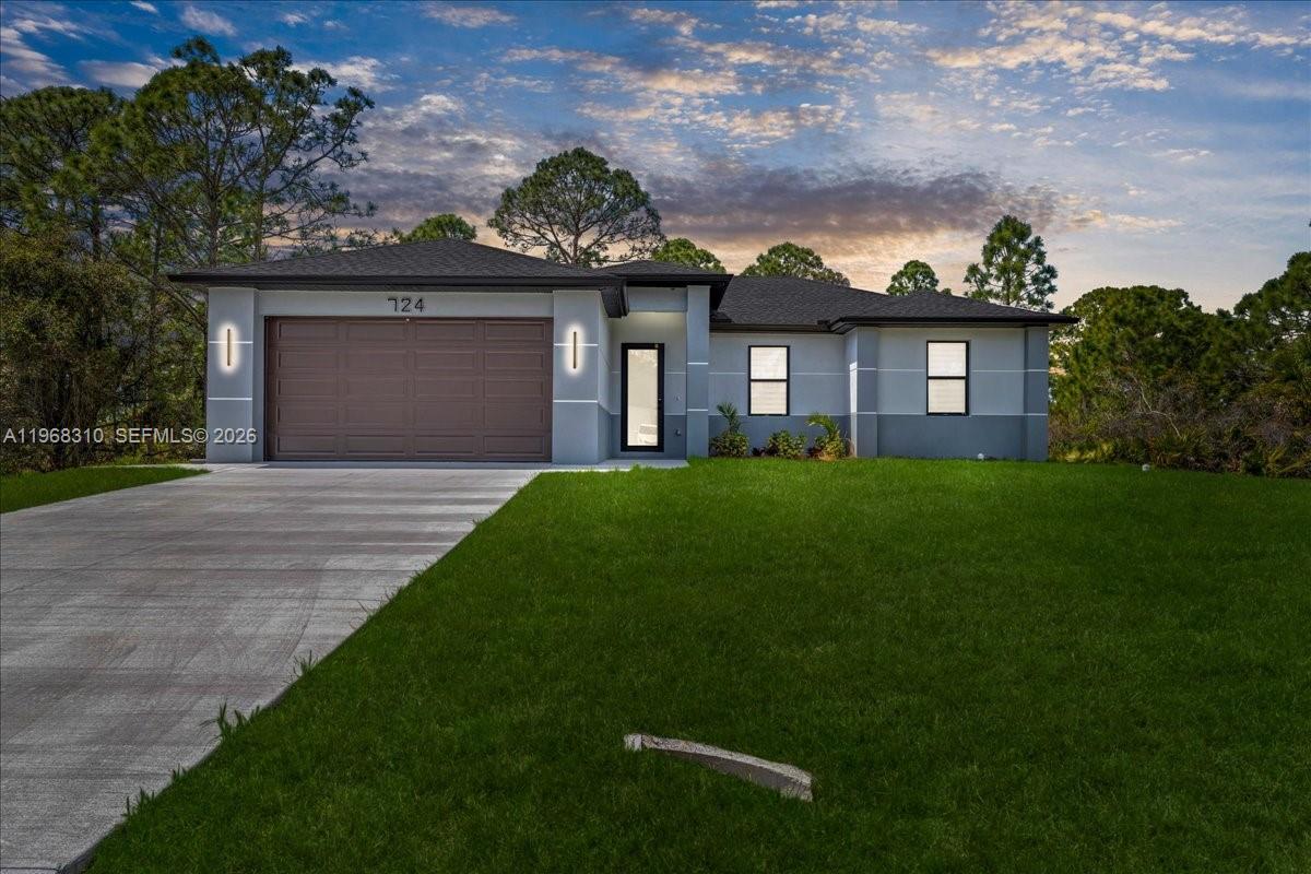 A single-story house with a two-car garage, gray stucco exterior, and a dark shingled roof — 724 Drury Ave, Lehigh Acres FL 33974, LEHIGH ACRES, FL