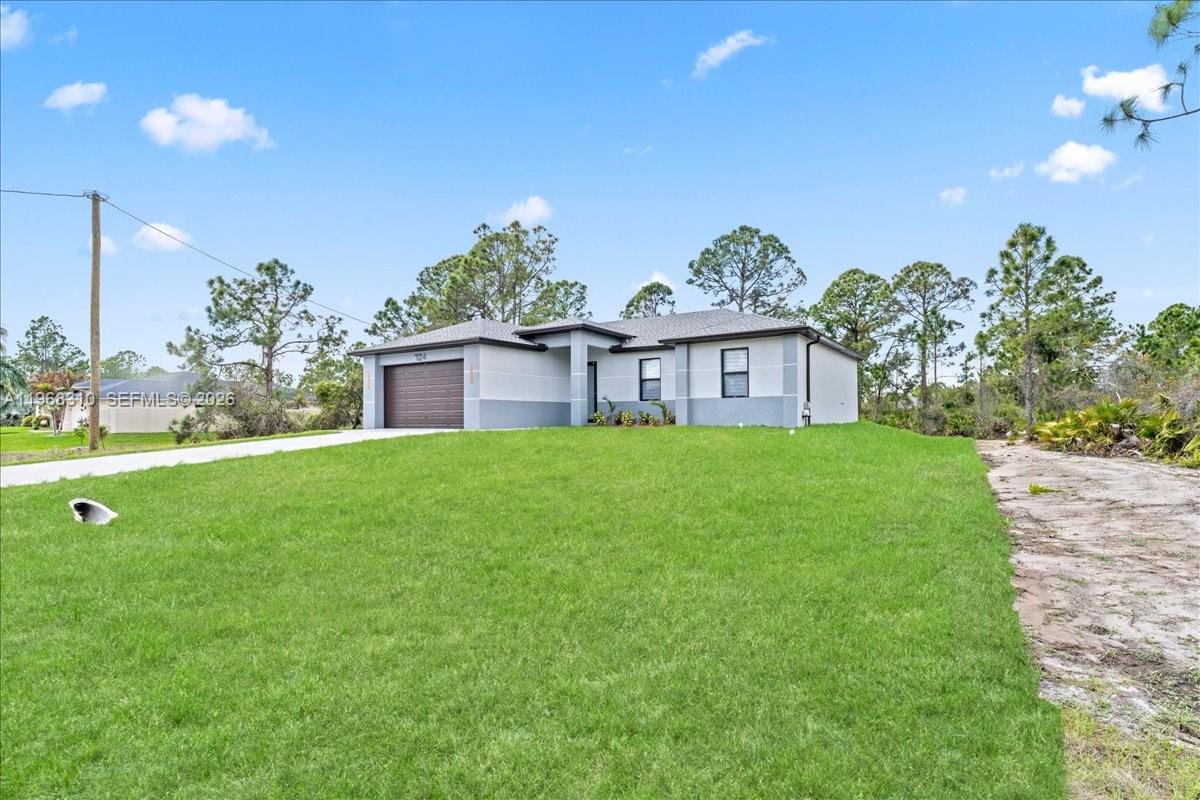 A single-story house with a brown garage and a large front lawn under blue skies — 724 Drury Ave, Lehigh Acres FL 33974, LEHIGH ACRES, FL