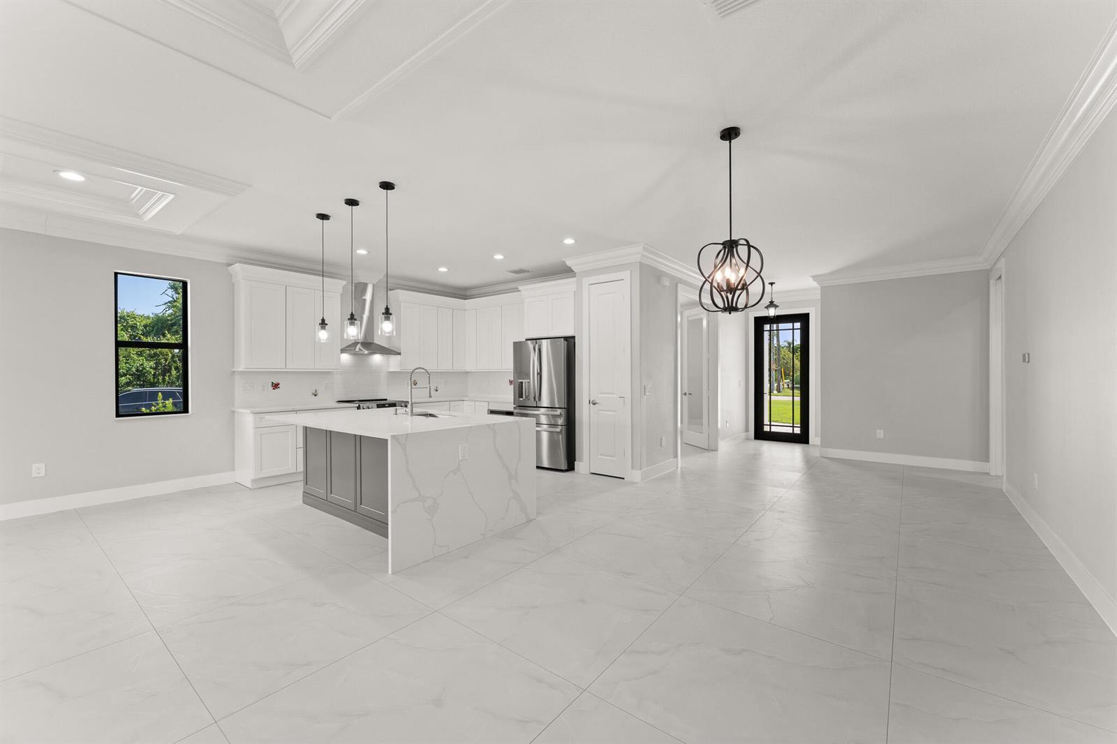 A modern kitchen features white cabinets, a gray island with a marble countertop, and tile flooring — 5460 SE Front Avenue, Stuart FL 34997, STUART, FL