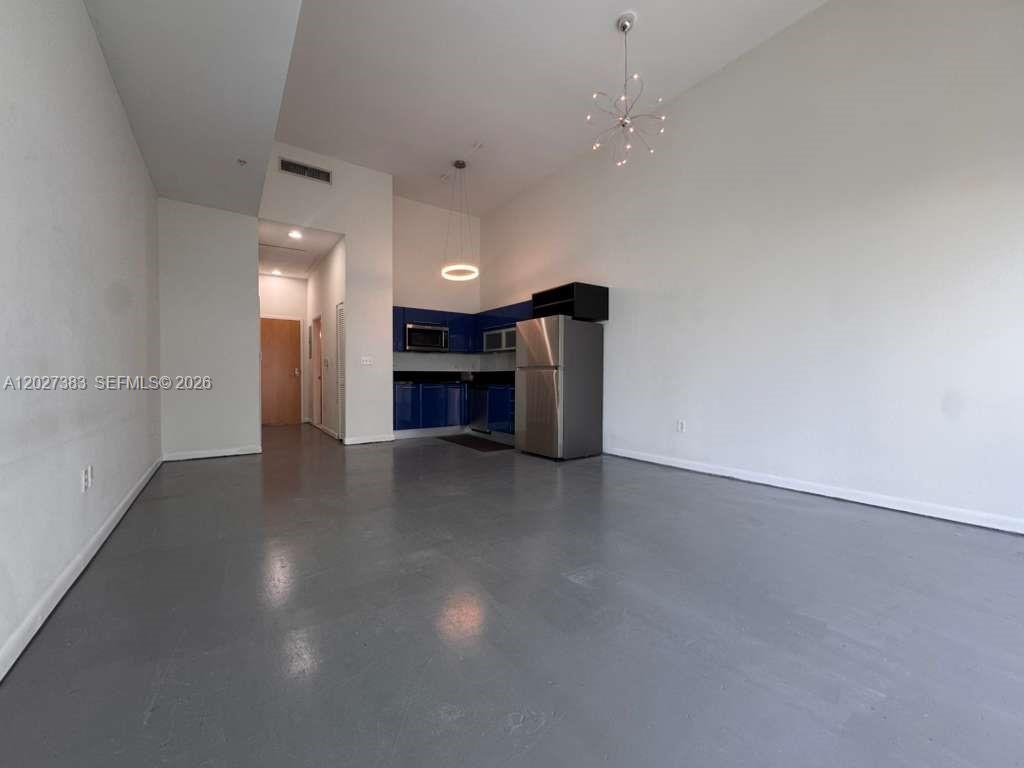 An open-concept room features a kitchen with blue cabinets, stainless steel appliances, and gray flooring — 253 NE 2nd St # 324, Miami FL 33132, MIAMI, FL