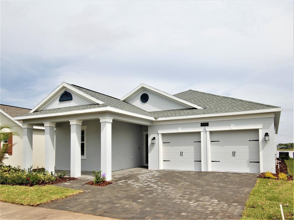 The rear exterior of a light-colored single-story house features a covered patio and lawn — 4619 RHYTHM ROAD, KISSIMMEE, FL