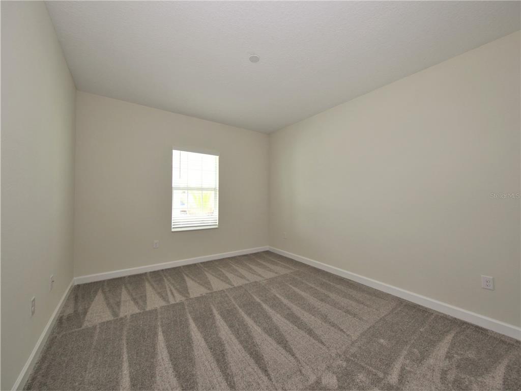 An empty bedroom features beige walls, gray carpet, and a single window with blinds — 4619 RHYTHM ROAD, KISSIMMEE, FL
