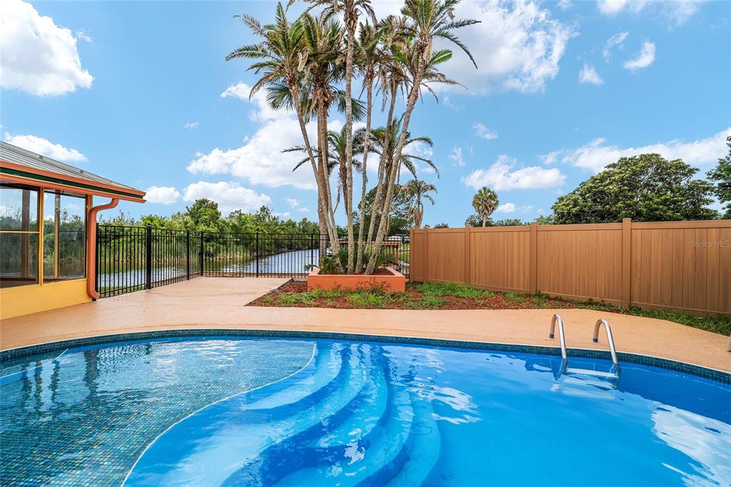 A swimming pool sits on a patio next to palm trees and a canal — 5330 KINGS COURT, FRUITLAND PARK, FL