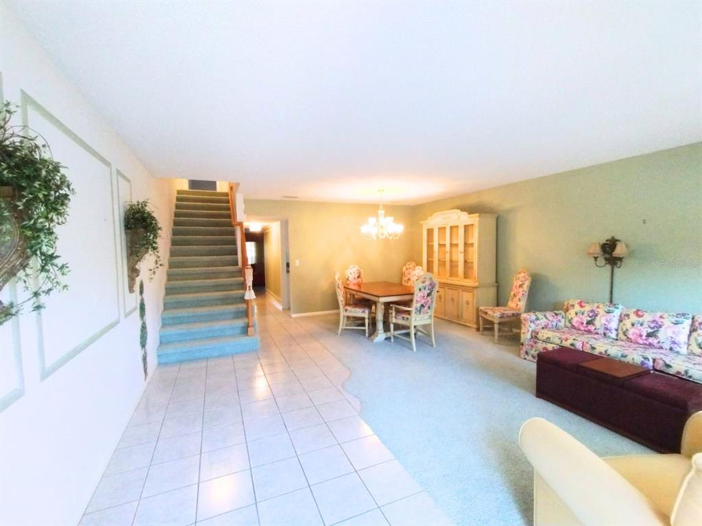 A living and dining area features a carpeted staircase, tile flooring, and floral furniture — 8830 SW 98 PLACE UNIT M, OCALA, FL