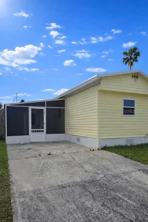 A yellow mobile home features a screened-in porch and a concrete driveway under a blue sky — 6726 ALBATROSS LANE, HUDSON, FL