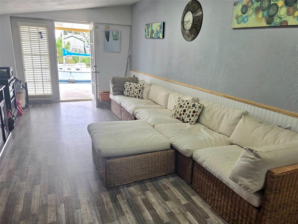 A living room features a large wicker sectional sofa, wood-look flooring, and a door to a dock — 6726 ALBATROSS LANE, HUDSON, FL