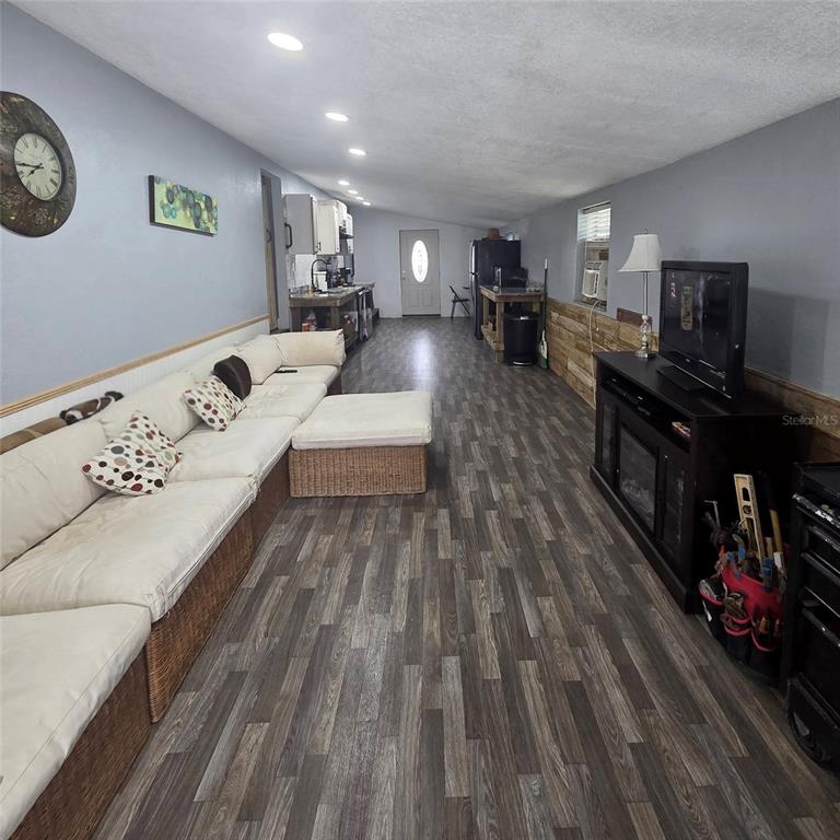 A long, narrow living room features wood-look flooring, a large sectional sofa, and a kitchen — 6726 ALBATROSS LANE, HUDSON, FL