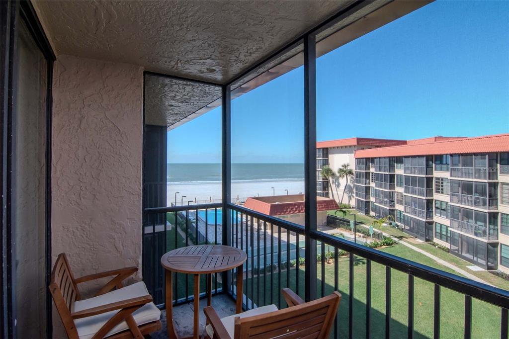 A screened balcony features a small wooden table and chairs overlooking the beach and ocean — 17580 GULF BOULEVARD UNIT 403, REDINGTON SHORES, FL