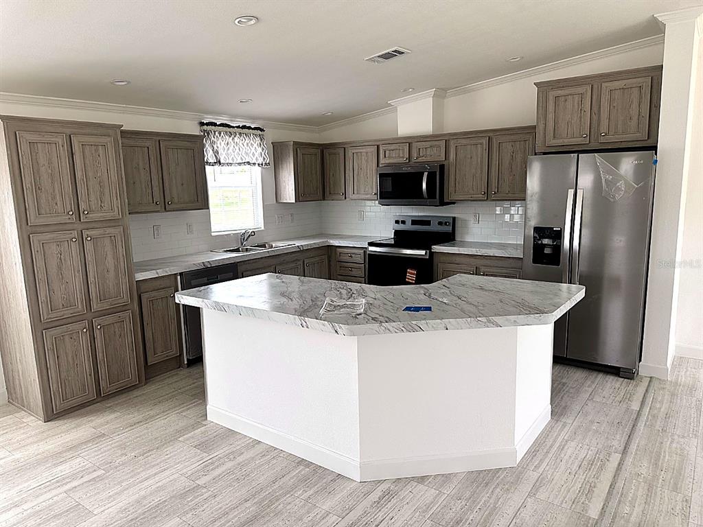 A kitchen features wood-toned cabinets, a white island with a marble-patterned countertop, and stainless appliances — 3492 GREENBLUFF ROAD UNIT 1119, ZELLWOOD, FL