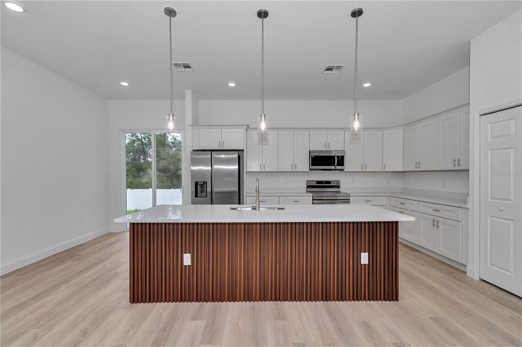 A modern kitchen features white cabinetry, a wood-slatted island, and stainless steel appliances — 17226 SW 20TH COURT ROAD, OCALA, FL