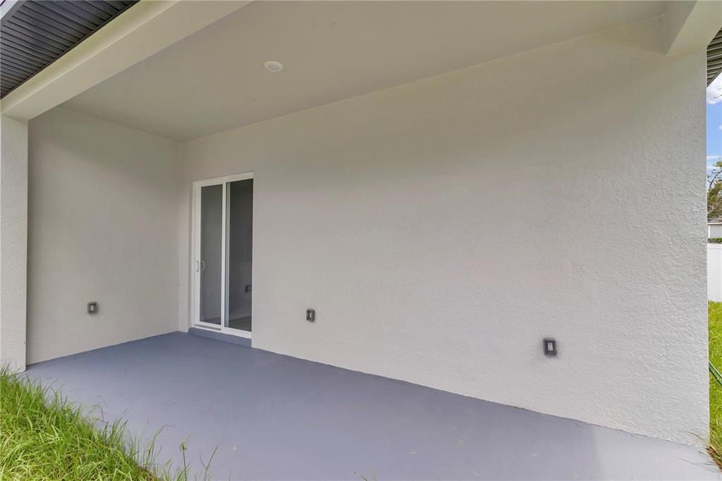A covered concrete patio with a sliding glass door and three exterior wall-mounted lights — 17226 SW 20TH COURT ROAD, OCALA, FL