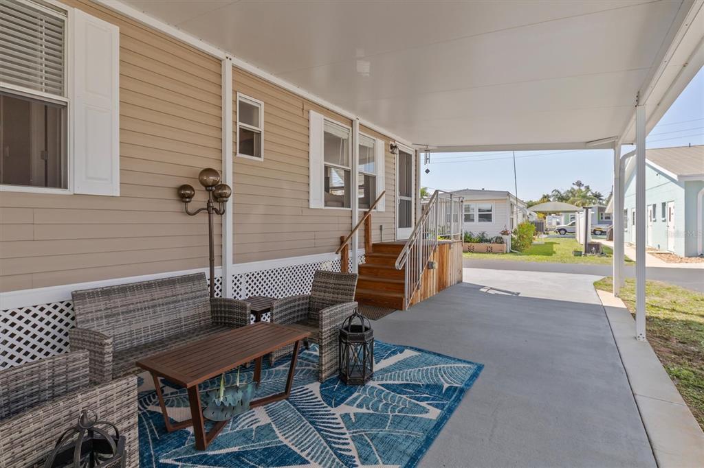 A covered concrete patio features wicker furniture, a patterned rug, and stairs leading to a home — 8320 RIVERSIDE DRIVE UNIT 51B, PUNTA GORDA, FL