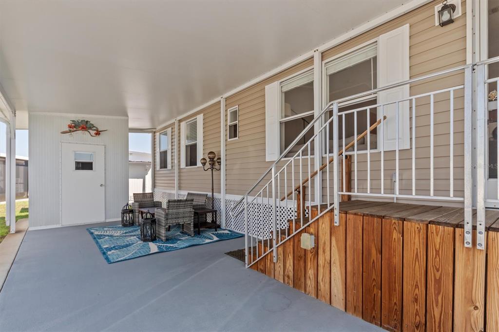 A covered patio features a gray concrete floor, wicker furniture, and wooden stairs with railings — 8320 RIVERSIDE DRIVE UNIT 51B, PUNTA GORDA, FL