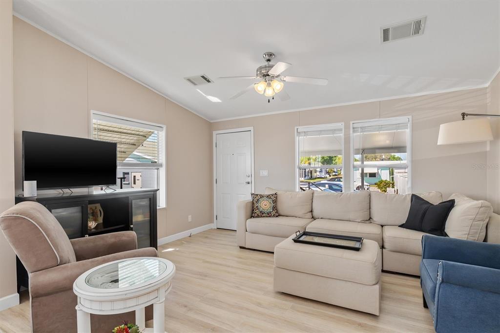 A living room features a sectional sofa, an armchair, a television, and light wood flooring — 8320 RIVERSIDE DRIVE UNIT 51B, PUNTA GORDA, FL