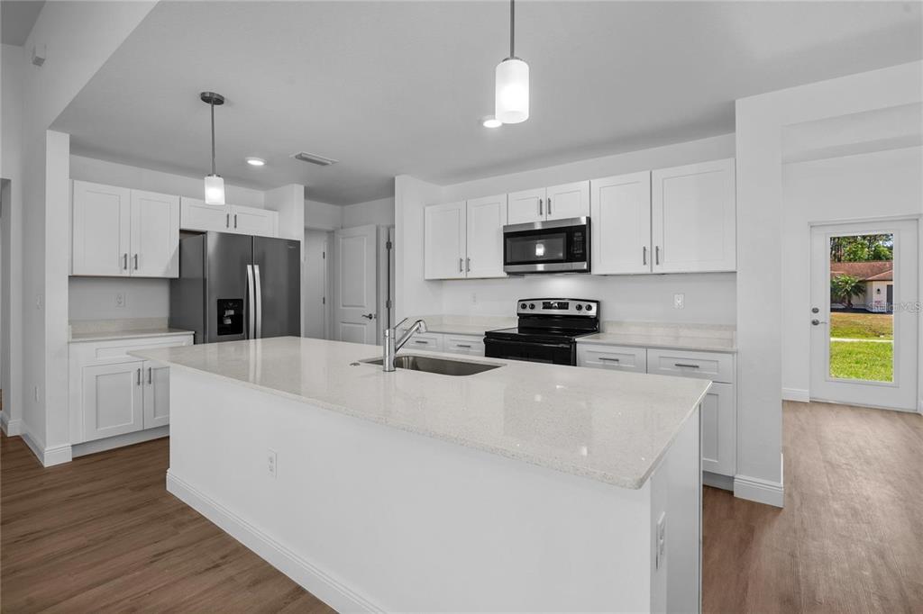 A modern kitchen features white cabinetry, a quartz island with a sink, and stainless appliances — 4442 ANTIOCH STREET, NORTH PORT, FL