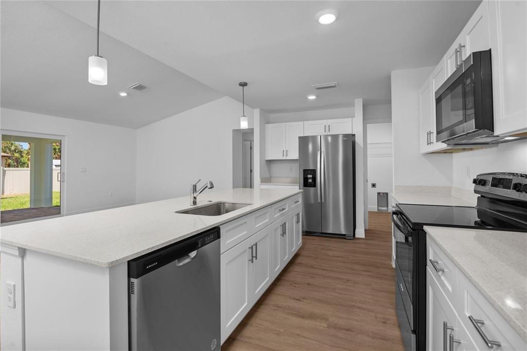 A modern kitchen features white cabinets, stainless steel appliances, a large island, and wood flooring — 4442 ANTIOCH STREET, NORTH PORT, FL