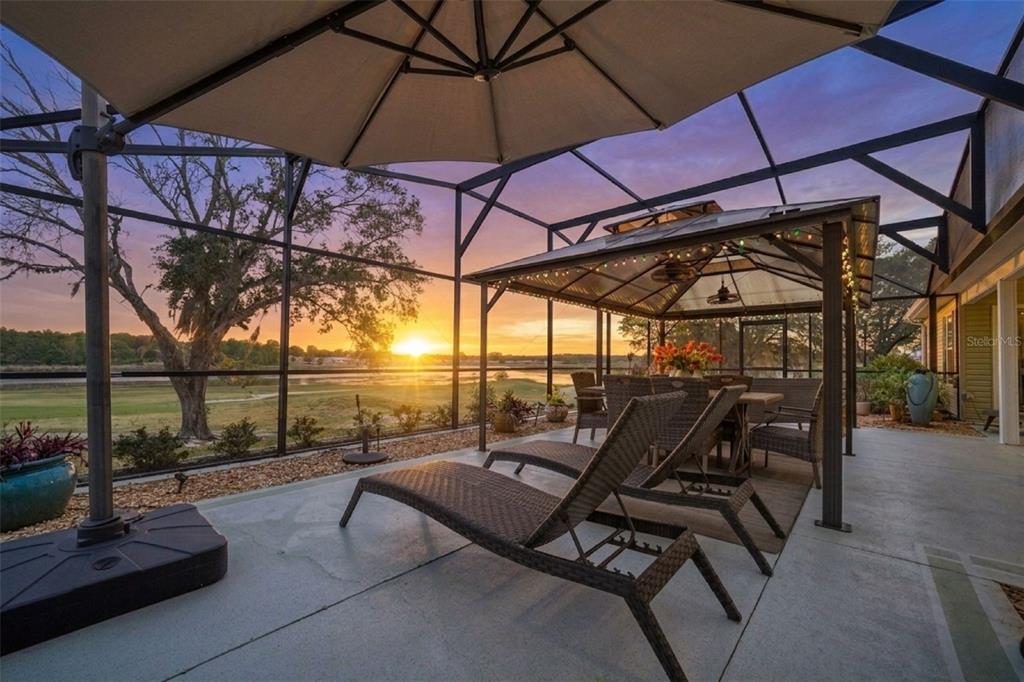 A screened-in patio features lounge chairs, a dining gazebo, and a sunset view of water — 4750 SAWGRASS LAKE CIR, LEESBURG, FL