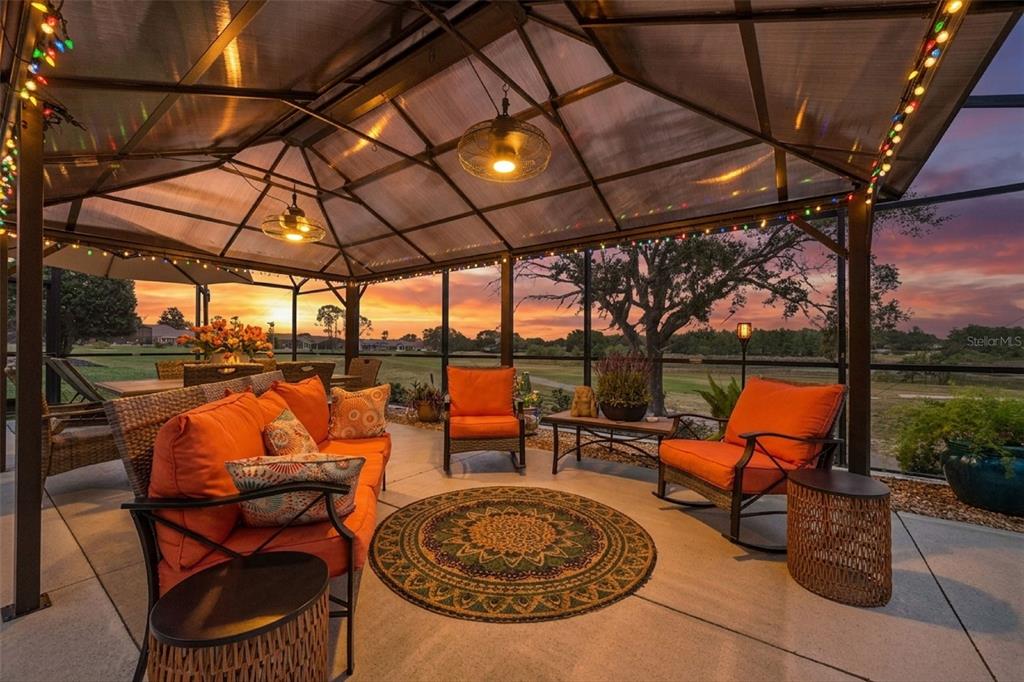 A screened-in patio features orange cushioned seating, a round rug, and a sunset view — 4750 SAWGRASS LAKE CIR, LEESBURG, FL