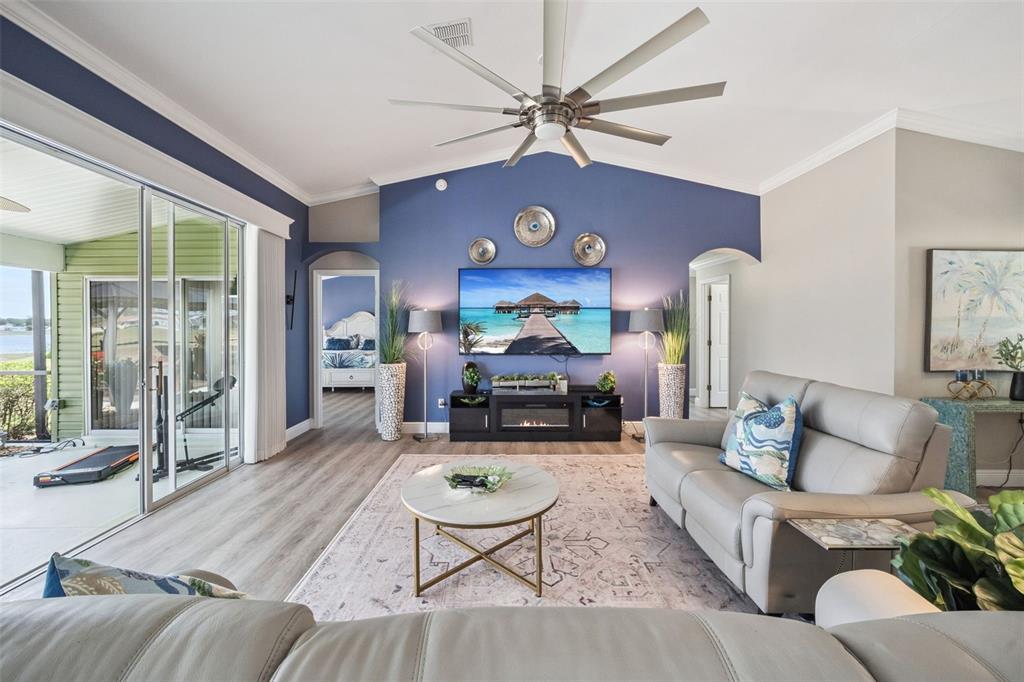 A living room features a blue accent wall, a large television, and light wood flooring — 4750 SAWGRASS LAKE CIR, LEESBURG, FL