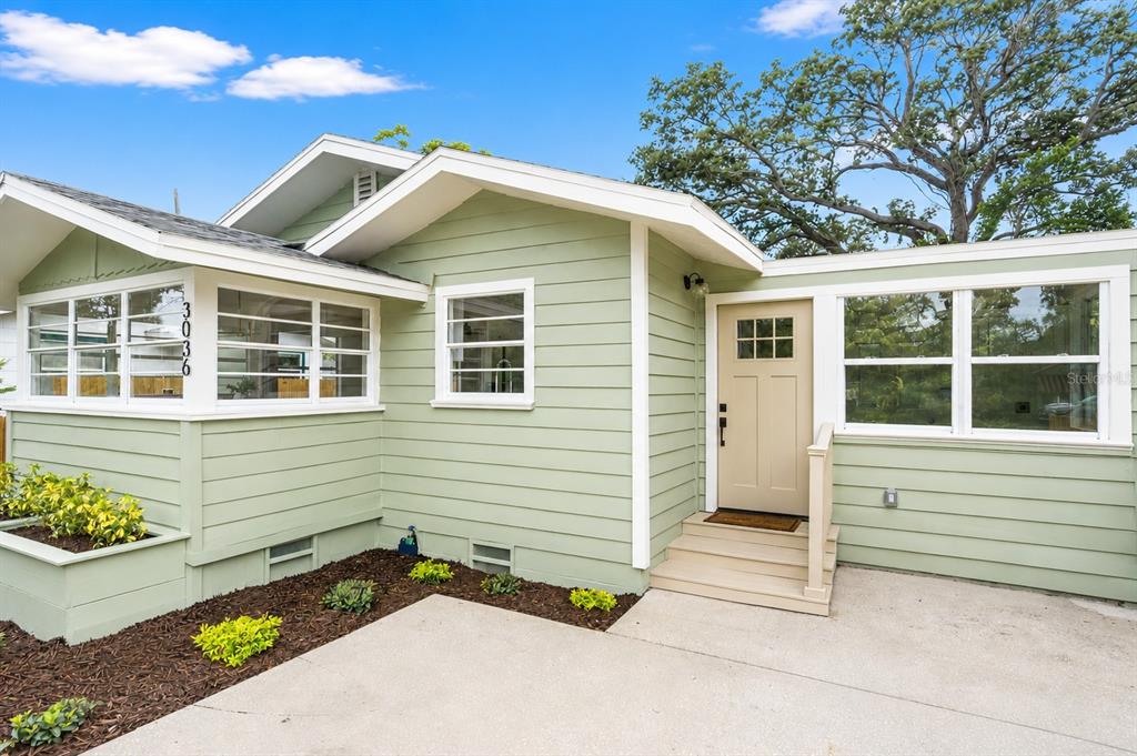 A light green house with white trim, a tan front door, and a concrete driveway — 3036 20TH STREET N, ST PETERSBURG, FL