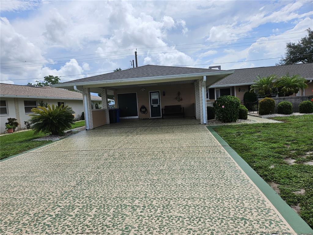 A single-story house features a large covered carport with a speckled concrete driveway — 1505 N PEBBLE BEACH BOULEVARD, SUN CITY CENTER, FL