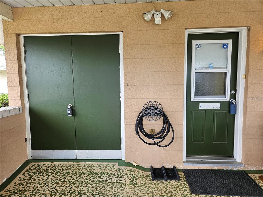 A covered porch features a green double door, a green entry door, and a wall-mounted hose — 1505 N PEBBLE BEACH BOULEVARD, SUN CITY CENTER, FL