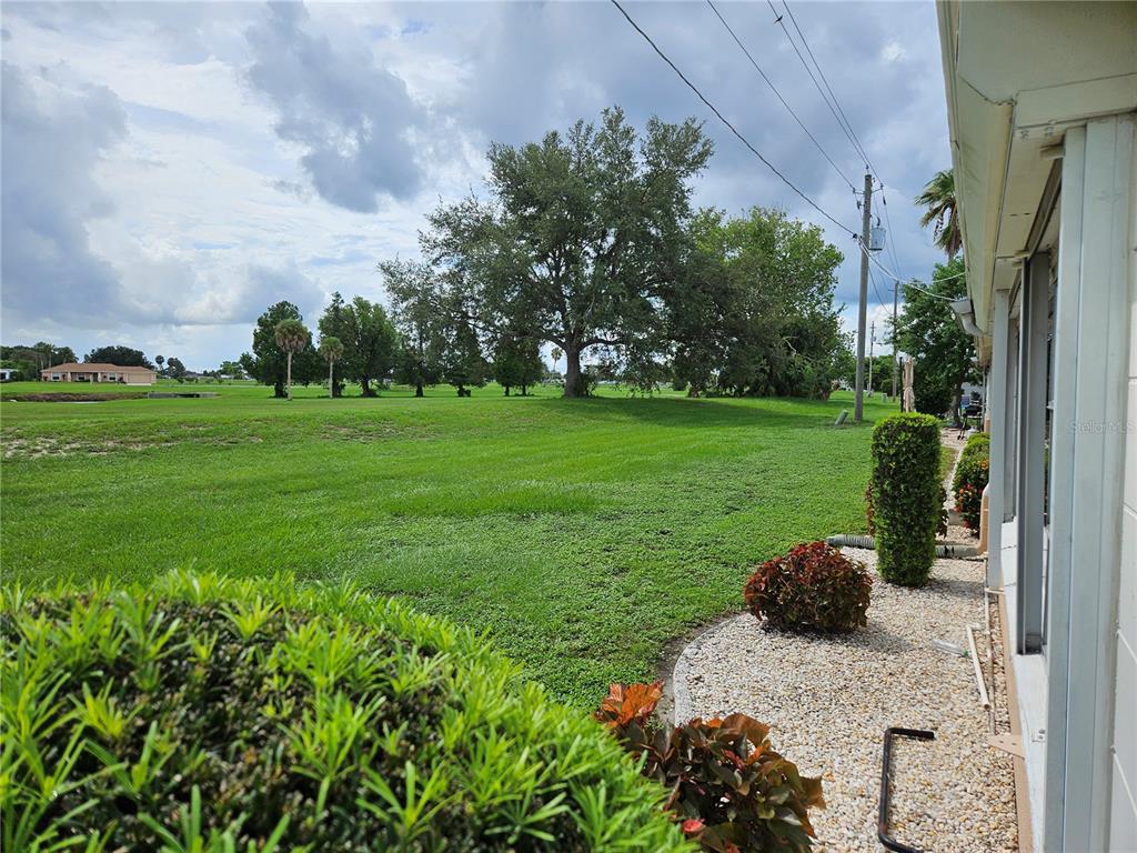 A view from a patio looking out over a large, grassy lawn with mature trees — 1505 N PEBBLE BEACH BOULEVARD, SUN CITY CENTER, FL