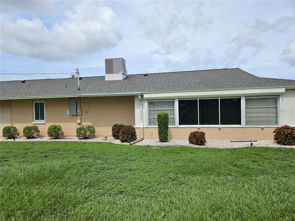 The exterior of a single-story house features a tan wall, a screened-in porch, and landscaping — 1505 N PEBBLE BEACH BOULEVARD, SUN CITY CENTER, FL