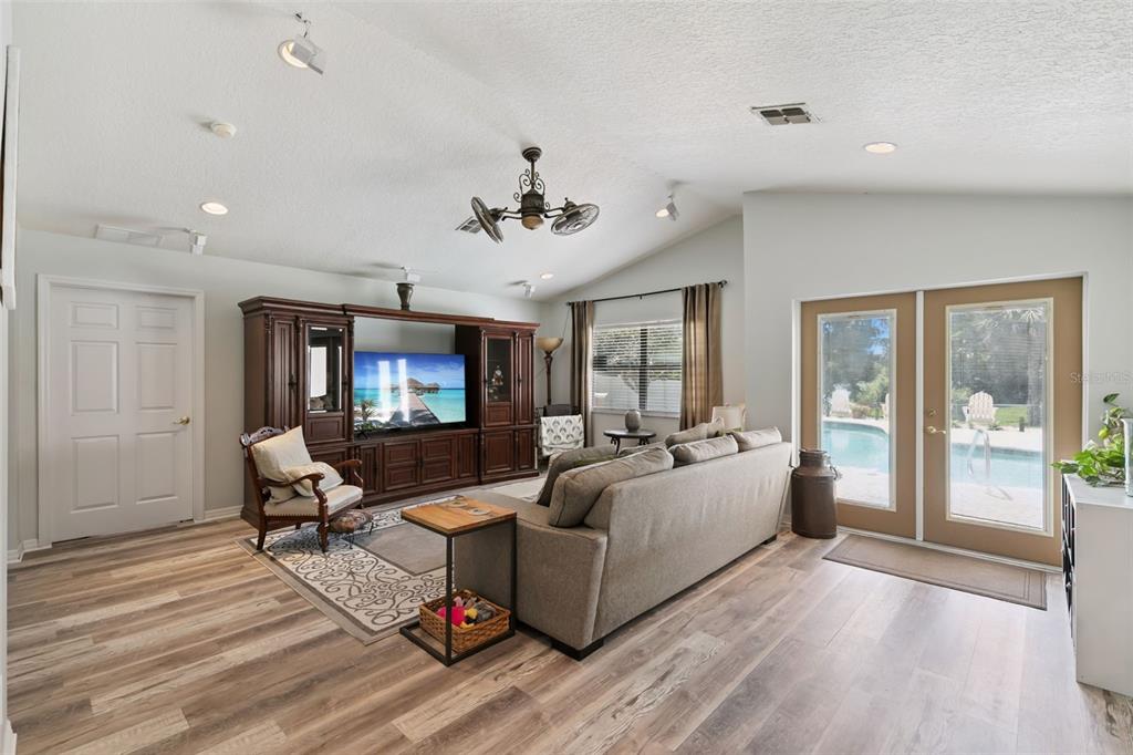A living room features wood-look flooring, a large entertainment center, a sofa, and glass doors — 1209 DEER RUN DRIVE, WINTER SPRINGS, FL