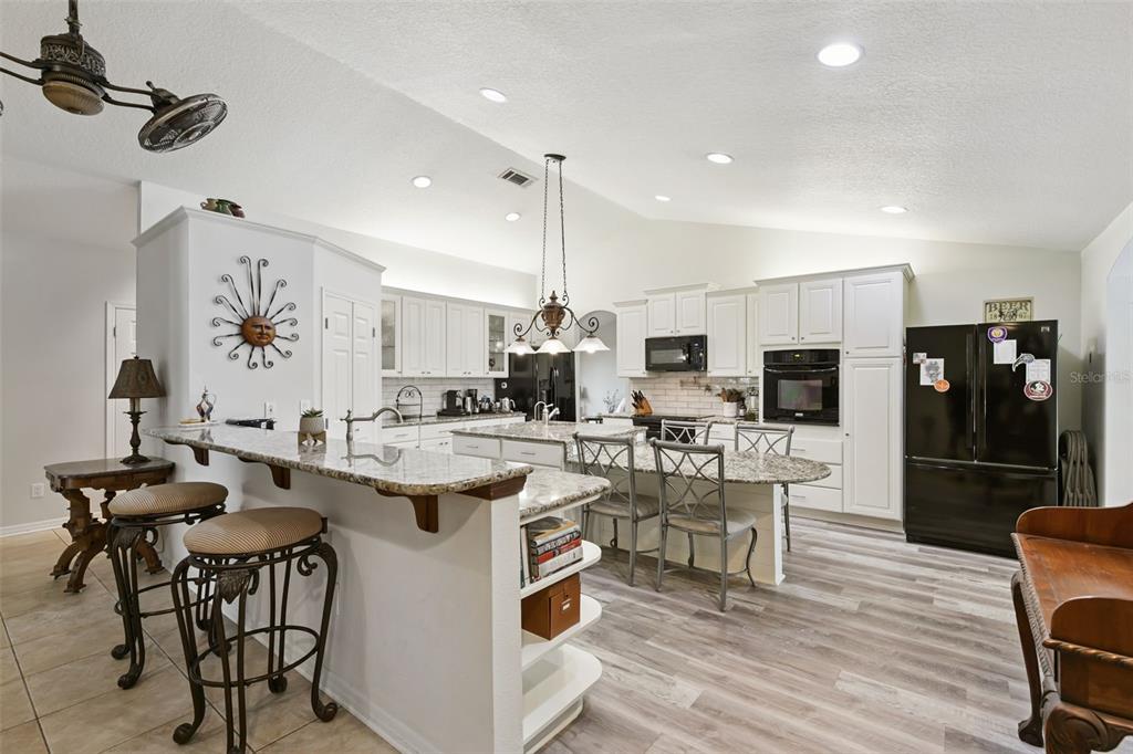 A kitchen features white cabinets, granite countertops, a breakfast bar, and light wood-look flooring — 1209 DEER RUN DRIVE, WINTER SPRINGS, FL