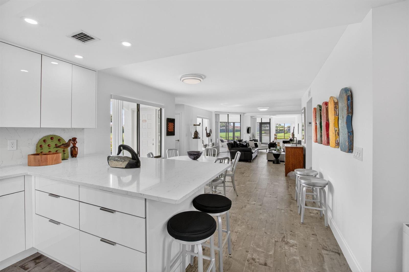 A modern white kitchen with a quartz island and bar stools overlooks an open living area — 15354 Strathearn Drive # 12601, Delray Beach FL 33446, DELRAY BEACH, FL