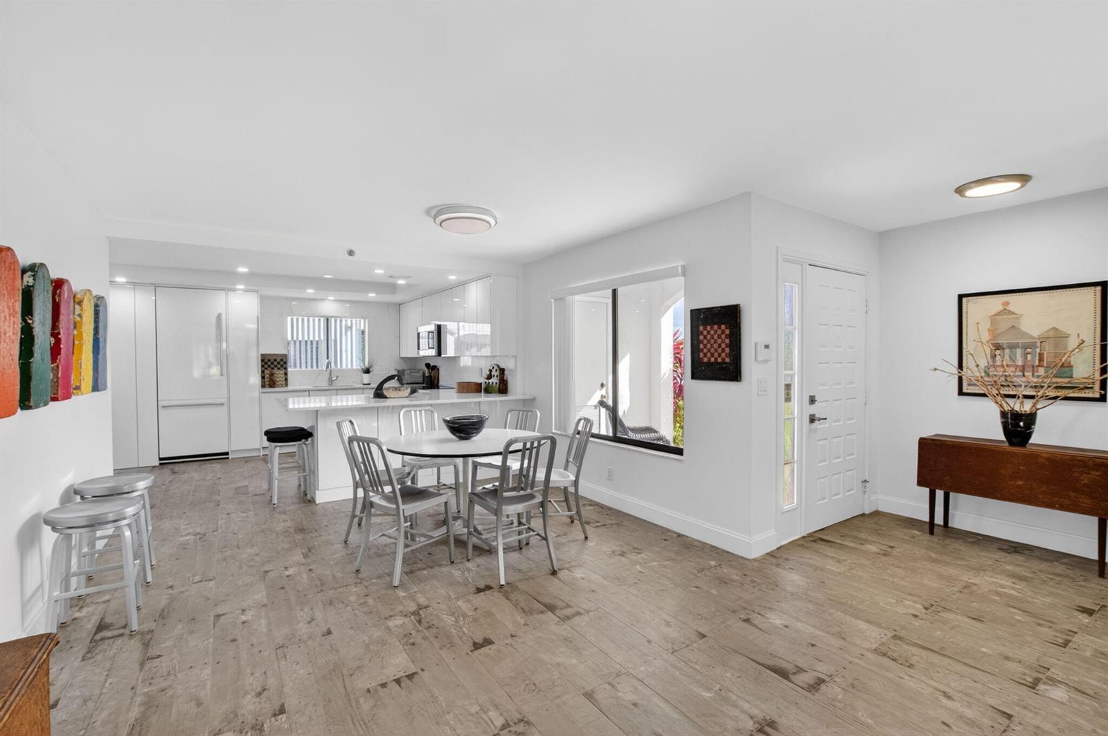 An open-concept kitchen and dining area features white cabinetry, metal chairs, and wood-look flooring — 15354 Strathearn Drive # 12601, Delray Beach FL 33446, DELRAY BEACH, FL