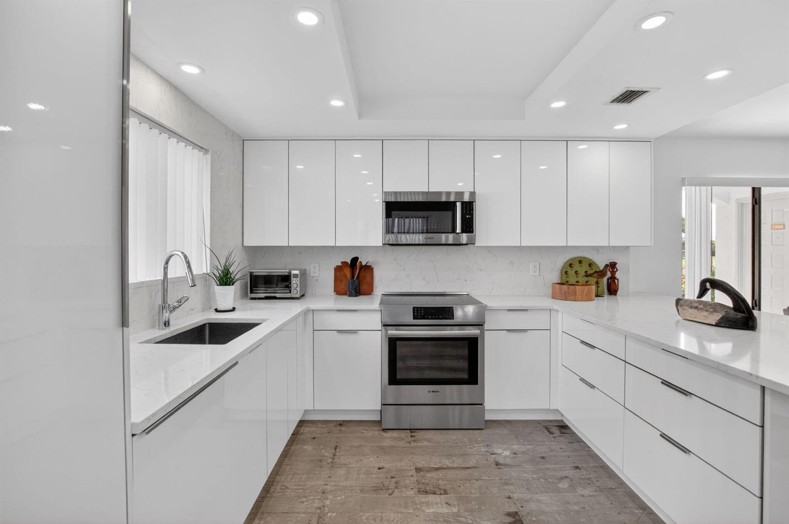 A modern kitchen features white flat-panel cabinets, stainless steel appliances, and light quartz countertops — 15354 Strathearn Drive # 12601, Delray Beach FL 33446, DELRAY BEACH, FL