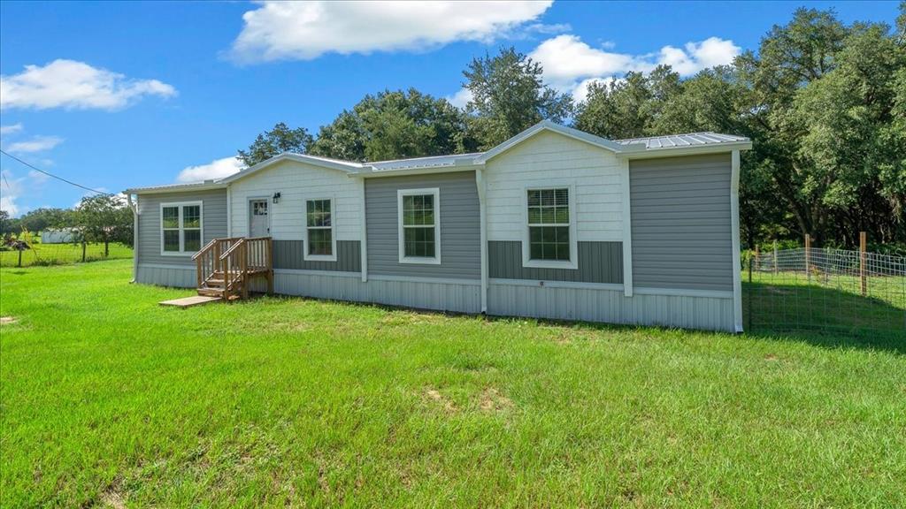 A single-story manufactured home with grey and white siding sits on a grassy lot — 14450 SE SUNSET HARBOR ROAD, WEIRSDALE, FL
